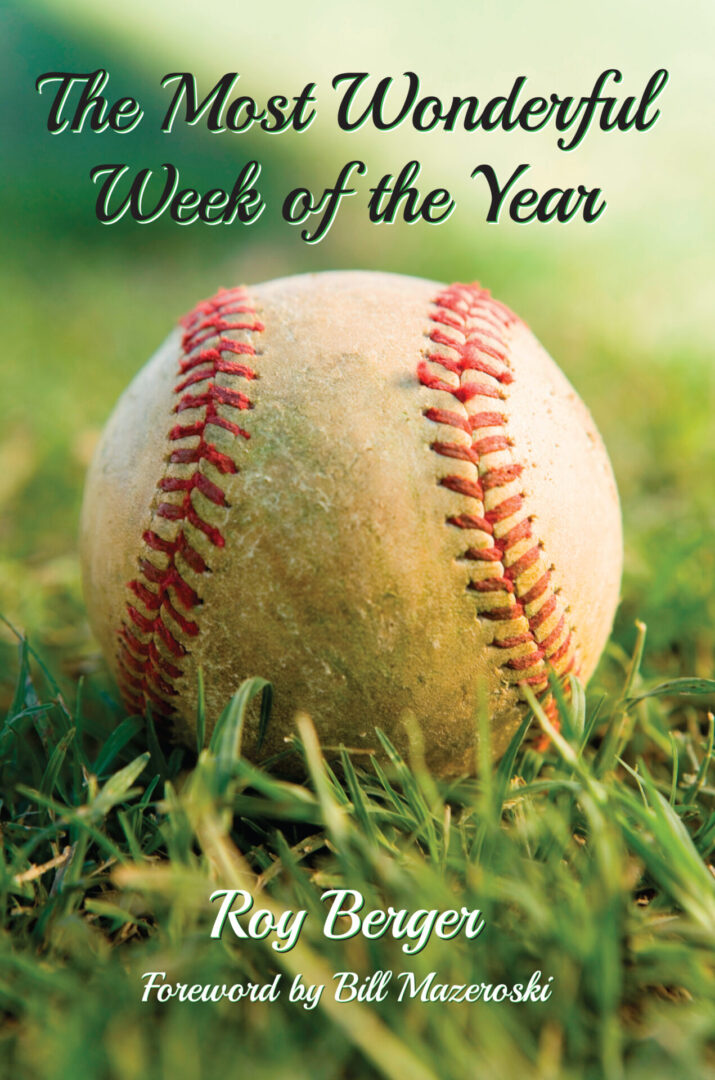 A well-used baseball lying on grass with The Most Wonderful Week of the Year by Roy Berger, featuring a foreword by Bill Mazeroski.