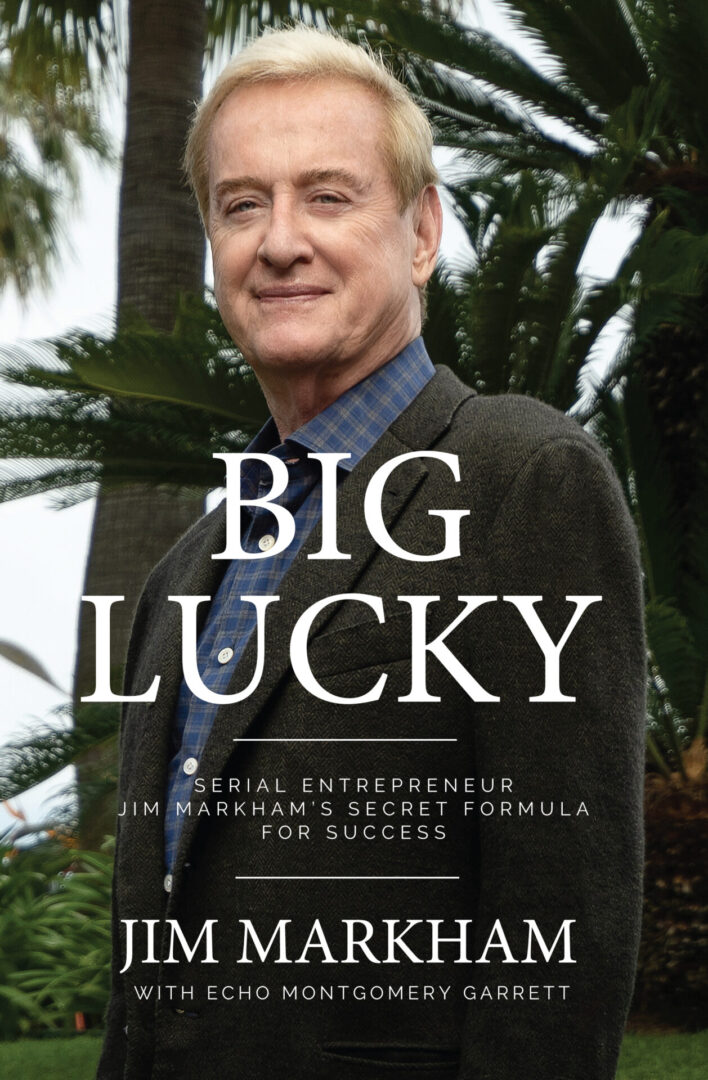 Man standing in front of palm trees with the title "Big Lucky" visible, referring to a book cover about Jim Markham, a serial entrepreneur.